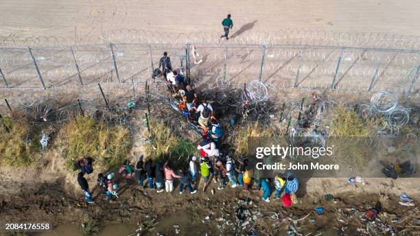 In an aerial view, immigrants pass through coils of razor wire while crossing the U.S.-Mexico border on March 13, 2024 in El Paso, Texas. The wire...