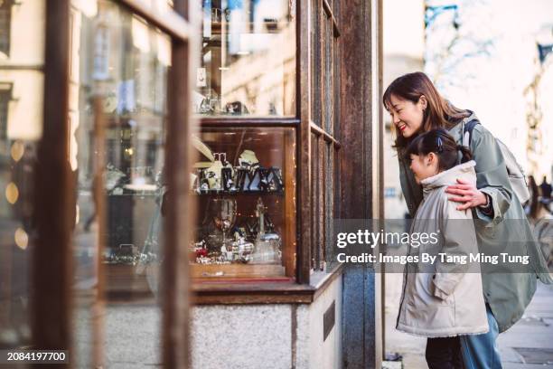 mom & daughter having window shopping outside a traditional antique shop while exploring in high street of a town - antique shop stock pictures, royalty-free photos & images