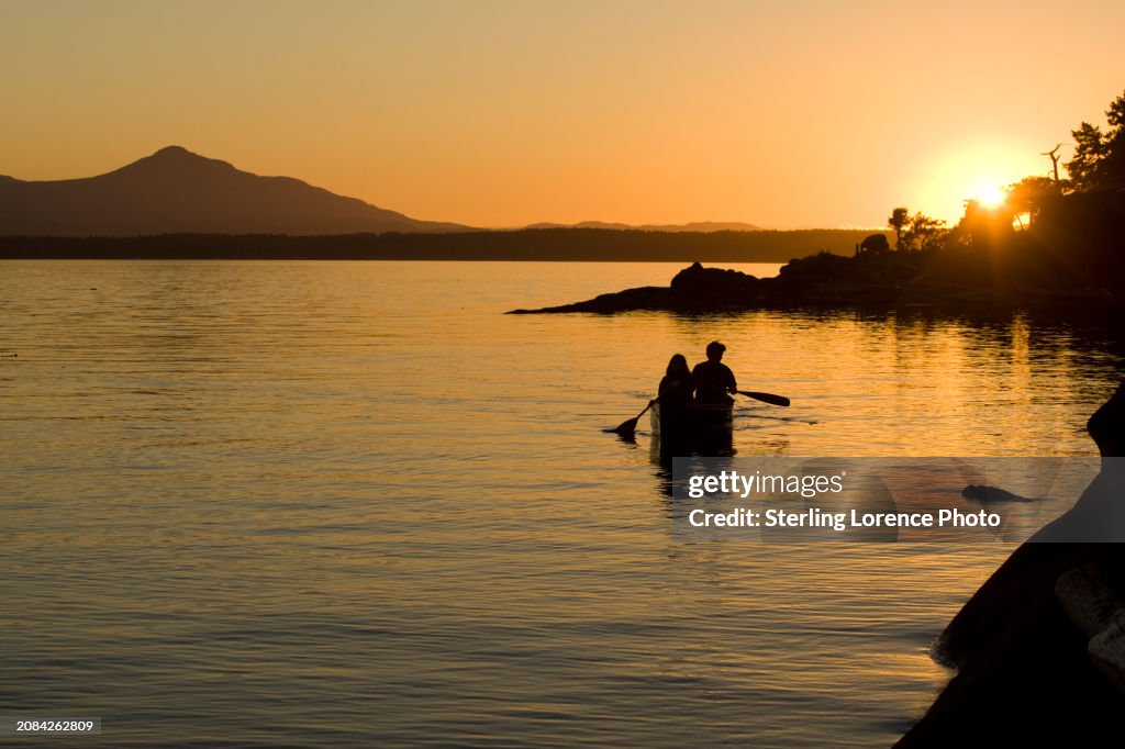 A couple goes for an evening work out paddling a canoe and to watch a dramatic sunset near recreational property in the gulf islands of British Columbia near Gabriola Island, Valdez island, Vancouver Island, Nanaimo. warm summer holiday