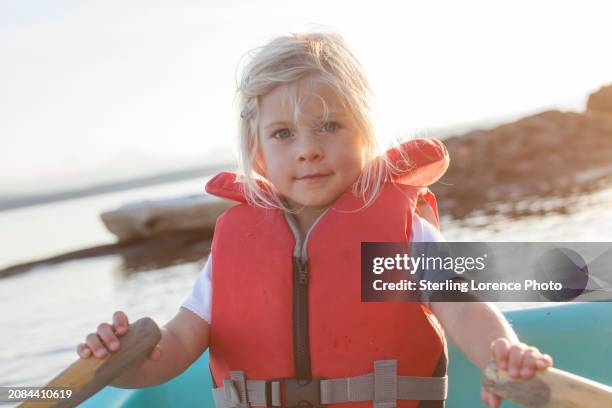 a young girl wearing a life jacket learning to row a dingy boat with oars  on a summer day during holiday in a sheltered bay in the gulf islands of british columbia near vancouver island, gabriola, salt spring island, galiano island - gabriola isle stockfoto's en -beelden