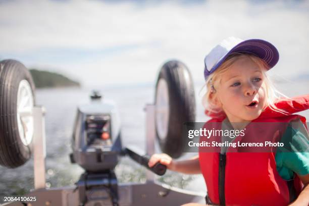 a young girl wearing a life jacket learning to drive a dingy boat with an outboard engine on a summer day during holiday in a sheltered bay in the gulf islands of british columbia near vancouver island, gabriola, salt spring island, galiano island - gabriola isle stockfoto's en -beelden