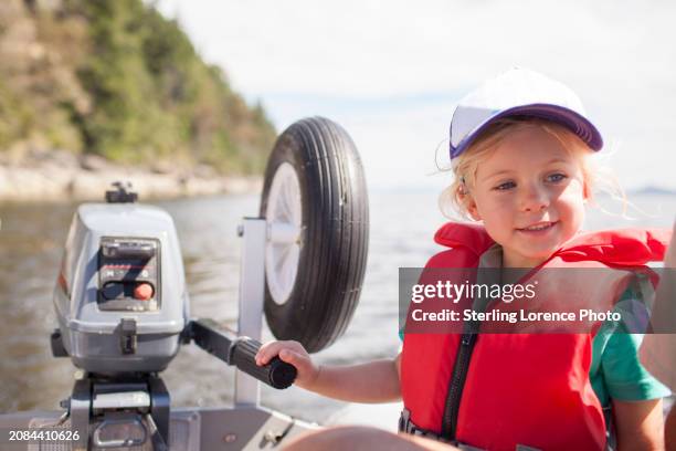 a young girl wearing a life jacket learning to drive a dingy boat with an outboard engine on a summer day during holiday in a sheltered bay in the gulf islands of british columbia near vancouver island, gabriola, salt spring island, galiano island - gabriola isle stockfoto's en -beelden