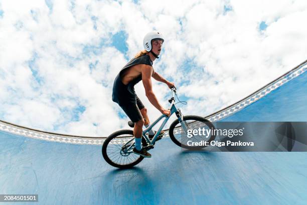 daring mid adult male cyclist riding the edge of a skate park bowl under a bright cloud-filled sky - training wheels stock pictures, royalty-free photos & images