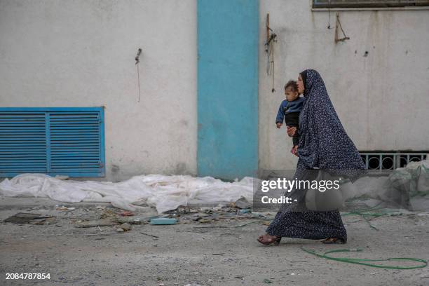 Woman carries her child and a bag of flour after humanitarian aid was distributed in Gaza City on March 17 amid ongoing battles between Israel and...