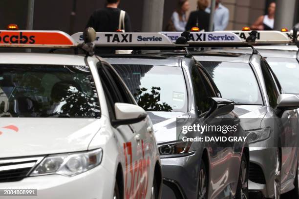 Pedestrians walk past a row of taxis in central Sydney on March 18, 2024. Australian taxi drivers impacted by the rise of ridesharing giant Uber have...