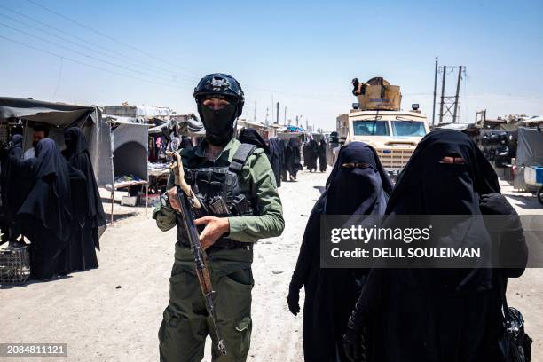 Women walk past a member of Kurdish security forces at the al-Hol camp in Syria's northeastern Al-Hasakah Governorate, on October 10, 2023. The...