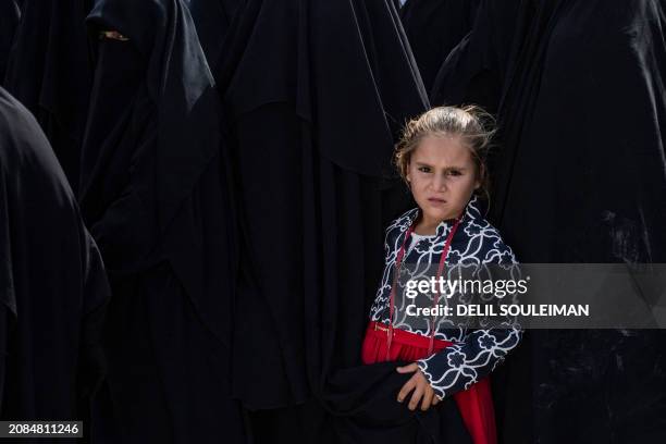 Girl stands with her mother as they gather next to a fence of the al-Hol camp in Syria's northeastern Al-Hasakah Governorate, on October 10, 2023....