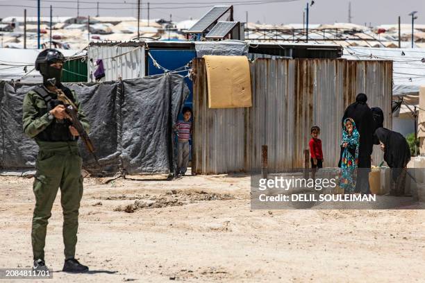 Member of Kurdish security forces stands guard as women and children fill water containers at the al-Hol camp in Syria's northeastern Al-Hasakah...
