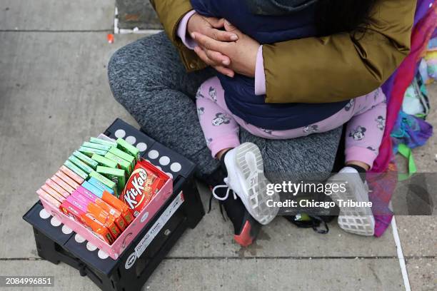 Migrant mother sells candy while holding her daughter at the corner of State and Washington streets in Chicago on Feb. 22, 2024.