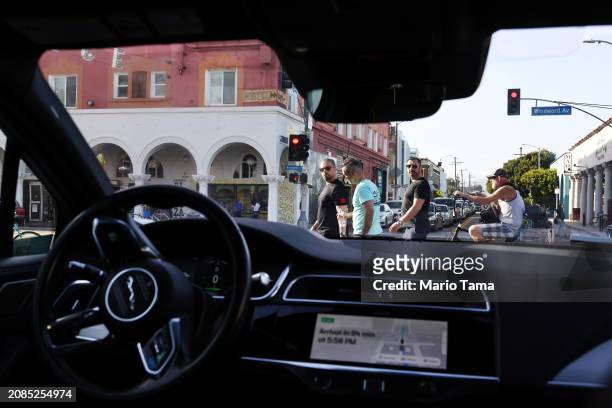 Pedestrians look toward a Waymo autonomous self-driving Jaguar taxi stopped at a red light near Venice Beach on March 14, 2024 in Los Angeles,...