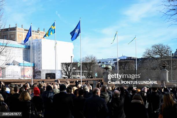 Members of the public stand under the flagsof the European Union, Sweden and NATO, as they attend a ceremony to mark Sweden's entry into NATO,...