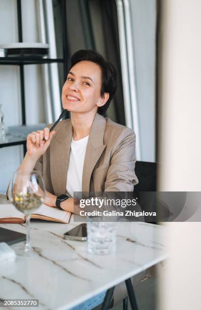 smiling young adult brunette woman in grey suit working at laptop in modern office - brunette sitting at desk stock-fotos und bilder