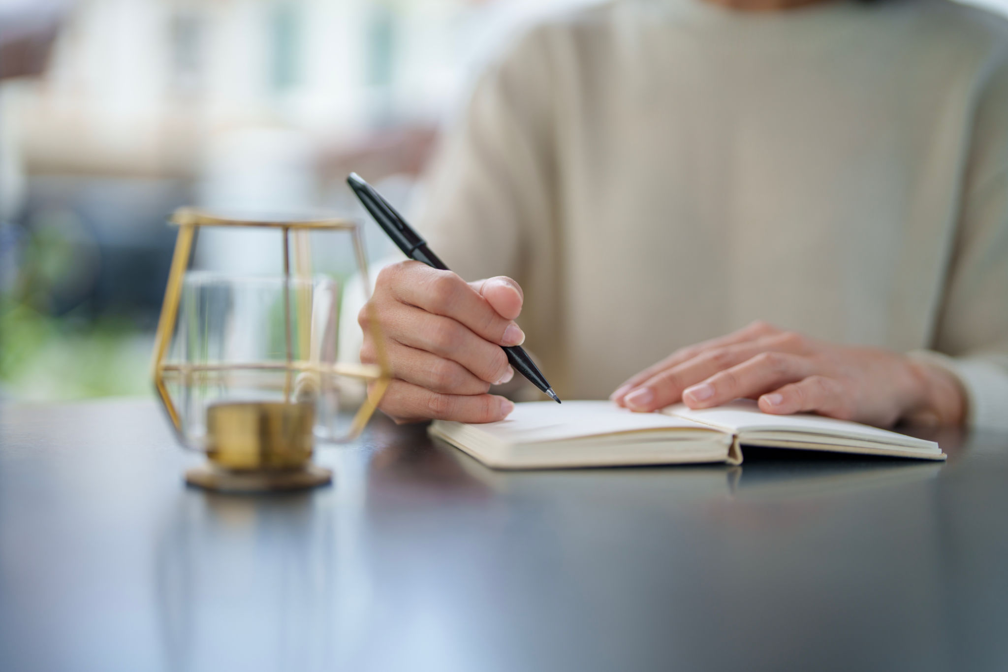 In the close-up shot, an Asian woman is seated at a table in her backyard, enjoying a moment of relaxation and me-time as she writes on a notepad in the morning. In the close-up shot, an Asian woman is seated at a table in her backyard, enjoying a moment of relaxation and me-time as she writes on a notepad in the morning.