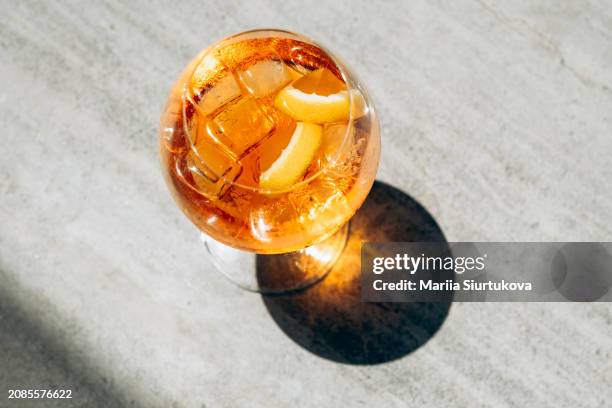 sunny aperitif. refreshing cocktail drink with citrus garnish, cast in the soft glow of sunlight, creates an inviting summer ambiance on a textured tabletop. - orange peel texture stock pictures, royalty-free photos & images