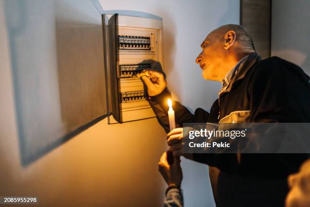 senior electrician checking fuses for customer at home, customer is holding candlelight - schakelaar stockfoto's en -beelden