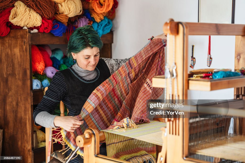 Female craftsman weaver weaving on a traditional wooden hand-loom in her workshop