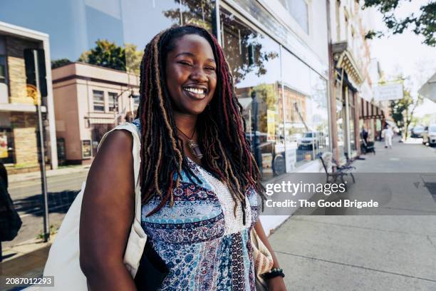 smiling young woman standing on sidewalk in downtown district - robe sans manches photos et images de collection