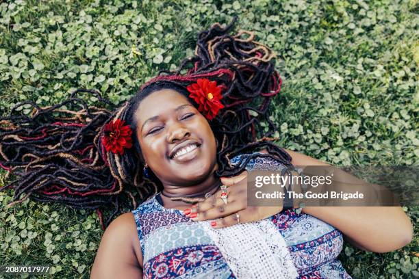cheerful young woman lying on grass with flowers in hair - hand over heart smiling stock pictures, royalty-free photos & images