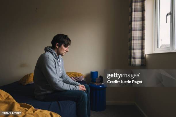powerful side view shot of a depressed mature man sitting on his bed - negative emotion - emotional wellbeing stock pictures, royalty-free photos & images