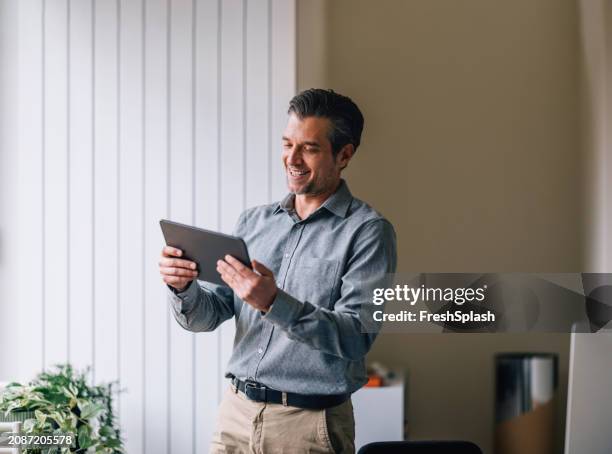 smiling businessman using digital tablet in modern office - chino stock pictures, royalty-free photos & images