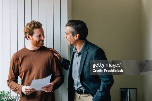 smiling young man and older man with document discussing in office - mentoria imagens e fotografias de stock