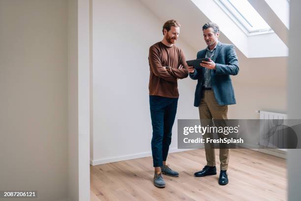 two professionals discussing work strategies on a tablet indoors - real estate agent stock pictures, royalty-free photos & images