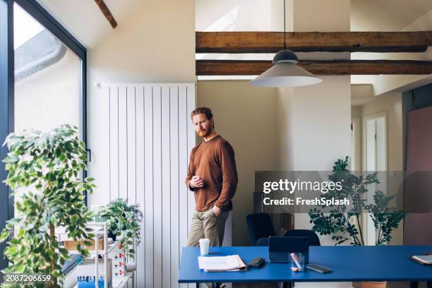 contemplative man standing alone in a stylish modern office - milestone stockfoto's en -beelden