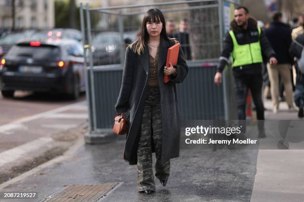 Guest seen wearing a grey long coat, brown shirt, cargo green pants, black heels, brown leather bag outside Lacoste Show during the Womenswear...