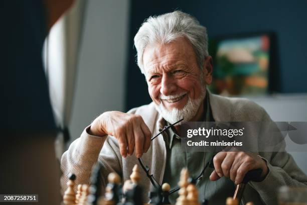 hombre mayor sonriente jugando al ajedrez con una enfermera anónima en la sala de estar - ajedrez fotografías e imágenes de stock