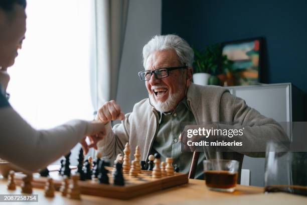smiling senior man playing chess with an anonymous nurse in the living room - nurses laughing stock pictures, royalty-free photos & images