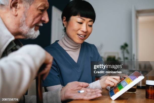 glückliche krankenschwester, die einem anonymen älteren mann im pflegeheim medikamente gibt - tablettenschachtel stock-fotos und bilder