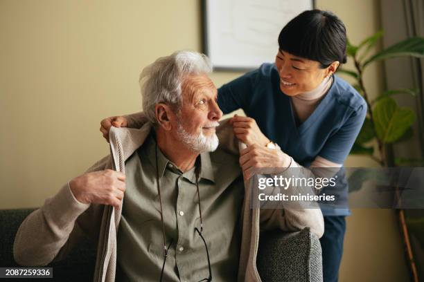 portrait d’un homme âgé et d’une aide-soignante asiatique l’aidant à enfiler une veste - se changer photos et images de collection
