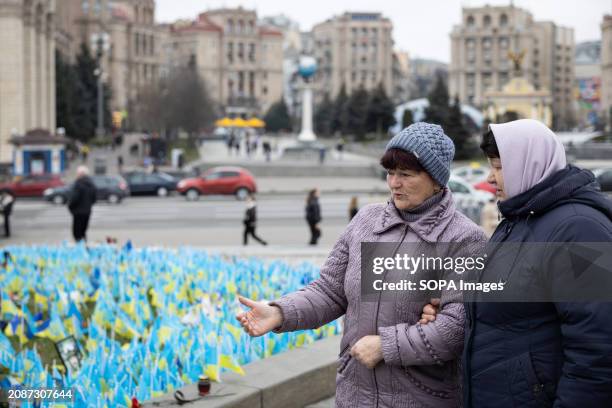 Women stand near an improvised memorial site on Independence Square in Kyiv, where relatives and friends plant Ukrainian flags with the names of...