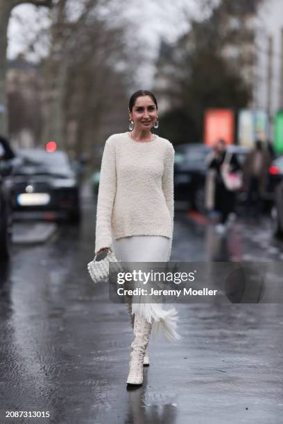 Geraldine Boublil is seen wearing a long white woollen sweater, an asymmetric knitted skirt with white fringes, high white boots with silver studs...