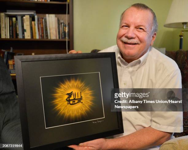 Paul Murray holds a symbol of the Baha'i faith, a framed Arabic calligraphic rendering known as "Greatest Name" at his home in Albany Thursday March...