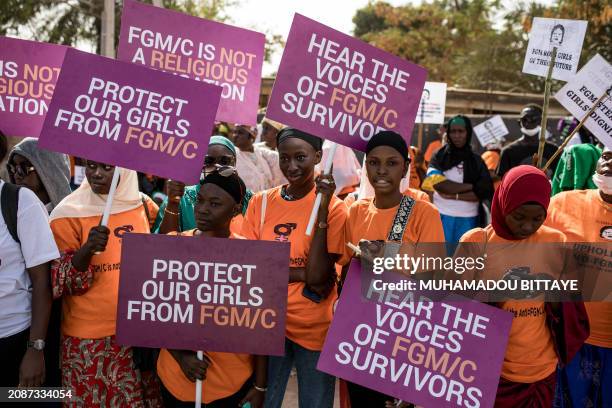 Anti Female Genital Mutilation protesters hold placards outside the National Assembly in Banjul on march 18 during the debate between lawmakers on a...