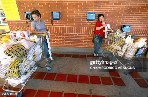 Two woman with carts full of food provisions wait for taxis at a supermarket in Caracas, 11 January 2003, on the 41st day of a general strike. Dos...