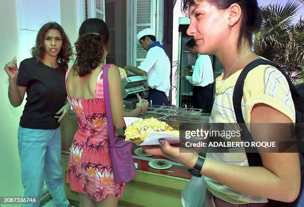 Young girls eat in front of a mexican taco stand, 23 April 2002 in Habana, Cuba. It is the first time that a state restaurant offers Meixcan food,...