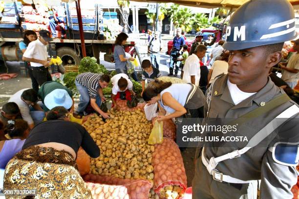 People select potatos to purchase, while they are patroled by a military oficial of the Venezuelan army, at the Mega Military Christmas and Town...