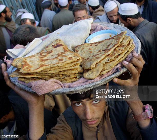 An Afghan boy bread seller balances a tray of naan on his head as he walks through a crowd of money changers at a money market in the Kabul, 29...