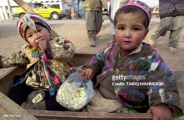 Two Afghan refugee toddlers eat popcorns while a food aid distribution by World Food Programme is going on at Jalozai refugee camp, 01 January 2002....