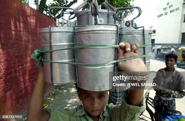 Salman Islam, a 12 year-old food vendor, carries lunch-boxes as he makes his way through a busy road in Dhaka, 05 July 2001, to reach his customers....
