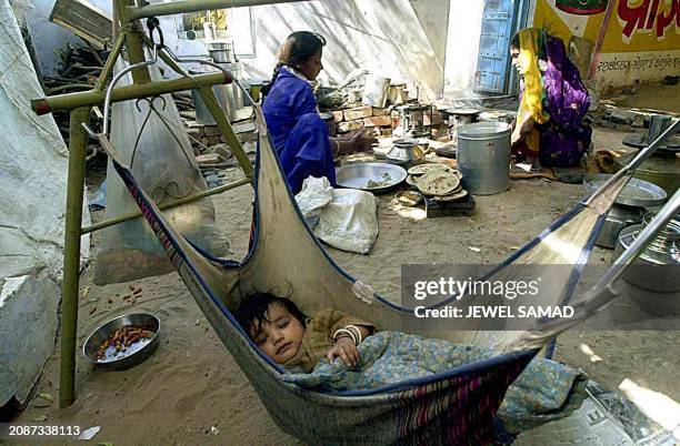 An Indian earthquake victim lies in a hammock as his mother and sister cook their food at their makeshift shelter beside the main road of Anjar 09...