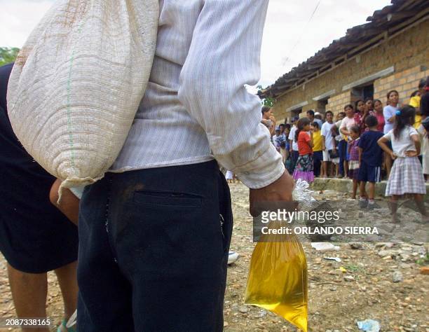 Woman carries bags of oil and grains as other inhabitants of San Jose, Honduras, stand in line to receive food aid from the United Nations World Food...