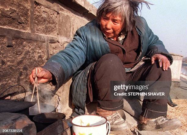 An homeless elderly woman stirs her watery cabbage soup in her makeshift shelter by a wall next to a canal 18 February in Beijing. Despite speeches...