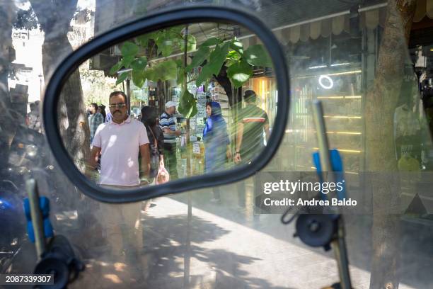 Bustling sidewalk reflected in the rearview mirror of a motorcycle, capturing the lively atmosphere and the flow of pedestrians in a Tehran street.