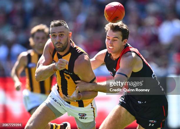 Jack Gunston of the Hawks handballs whilst being tackled by Zach Reid of the Bombers during the round one AFL match between Essendon Bombers and...
