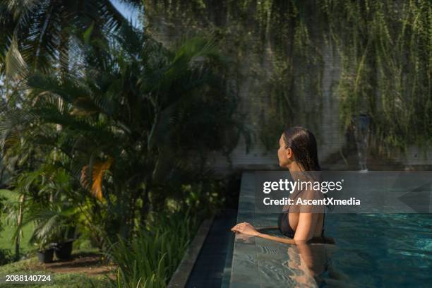 young woman relaxes on edge of swimming pool - escaping stock pictures, royalty-free photos & images