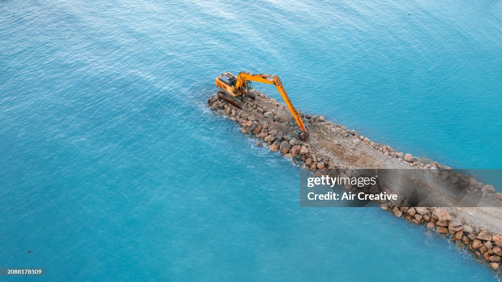 Aerial view of a crawler excavator on a stone jetty projecting into the sea, Alpes-Maritimes, France