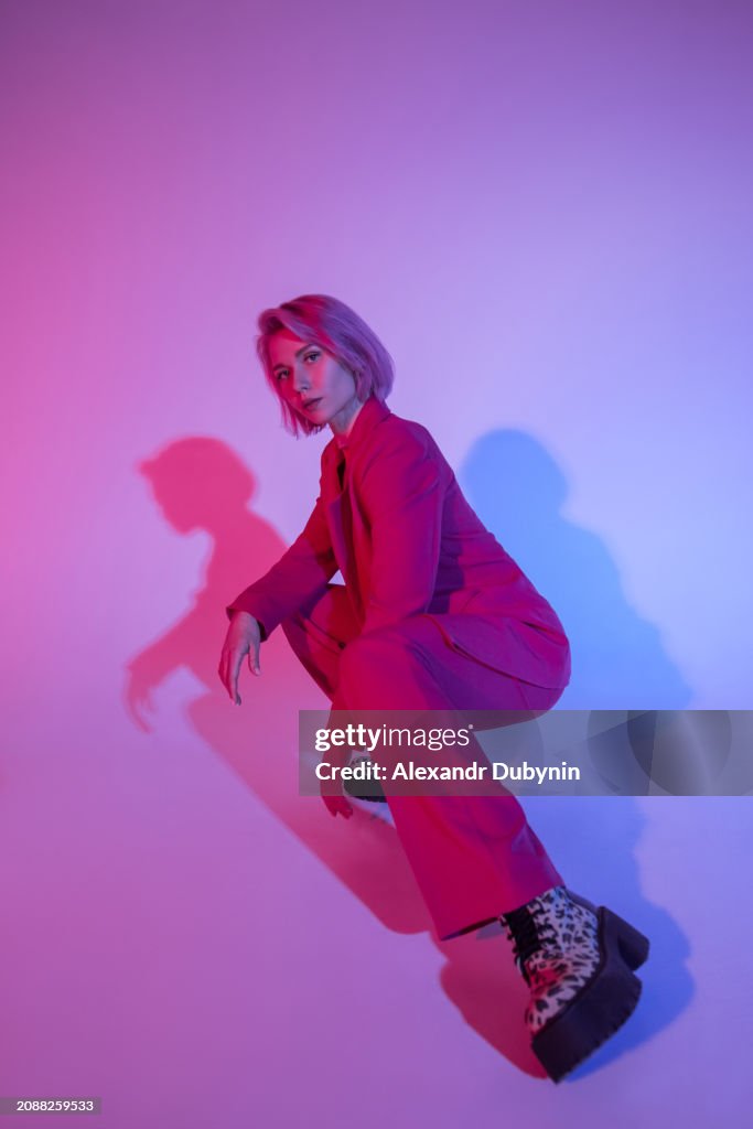 Fashionable woman posing squatting studio shot in neon light. Fashion concept